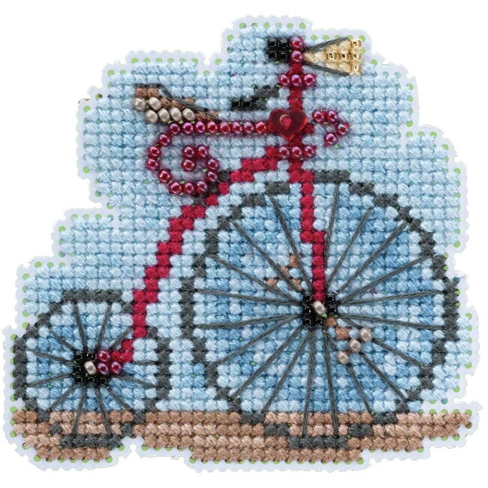 A cross stitch kit depicting a vintage bicycle with beads and floss on a fabric surface.
