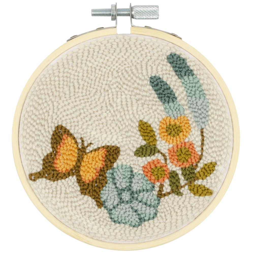 A bright and botanical punch needle kit by Needle Creations featuring a colorful butterfly landing on a blooming flower. The kit includes a 6-inch plastic locking embroidery hoop, a pre-printed 100% polyester fabric panel, vibrant yarn for the 3D loops, embroidery floss for fine details, a sewing needle, and easy-to-follow instructions