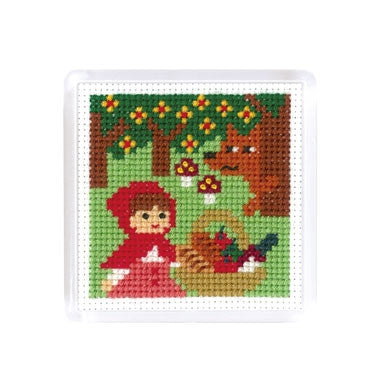 A cross stitch magnet featuring fairy tale characters little red riding hood with her basket of food and wolf lurking in the woods.