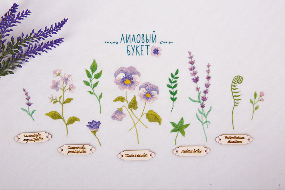 A series of embroidered violet flower designs with their scientific names, completed in different colors on a white background, with a label in the background providing information about the kit.