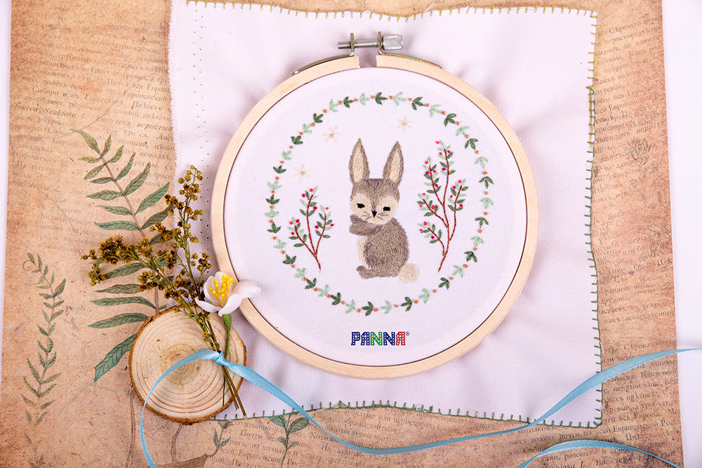Embroidery kit depicting a grey bunny with flowers in the background, on a white fabric surface, with branding 'Panna' visible.