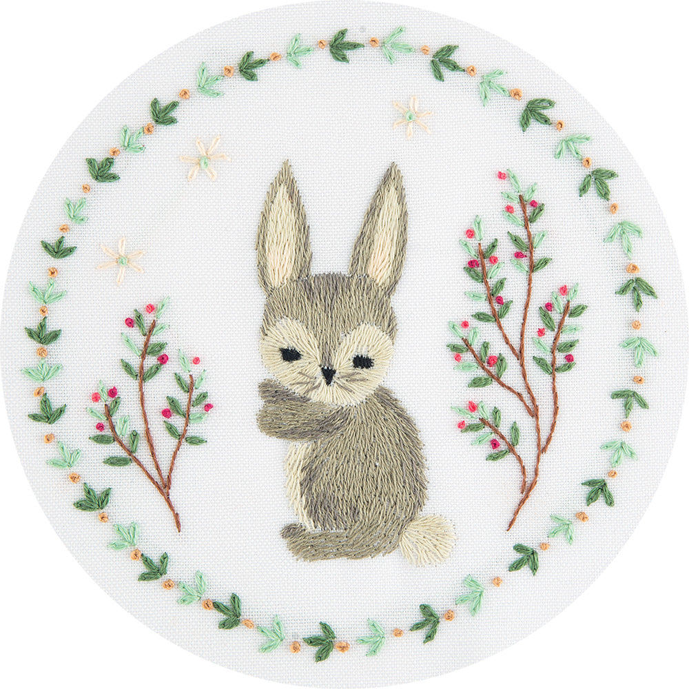 A miniature animal embroidery kit by Panna featuring a detailed 'Grey Bunny.' The kit includes fabric with a pre-printed design of a soft grey rabbit, a curated palette of embroidery threads for realistic fur shading, a needle, and instructions. The finished embroidery is a compact 10cm square, highlighting the bunny's gentle features and symbolic presence