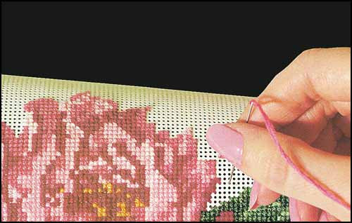 A close-up of a hand using a needle to perforate paper with a floral pattern design.