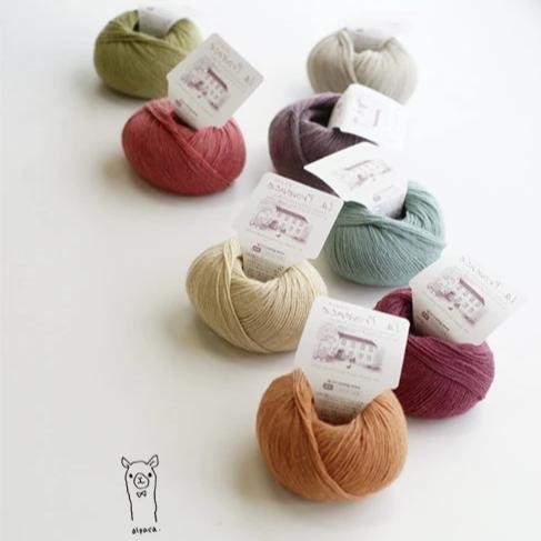 A delicate 30g skein of Pierrot Chiffon yarn in various soft pastel shade, showcasing its 100% pure alpaca fibers and ethereal halo.

A collection of colorful yarns in various colors, neatly placed in a line, with a label attached to one of the skeins.