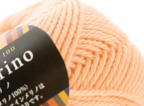 A 30g donut-style ball of Pierrot Fine Merino yarn. The image showcases the smooth, tightly spun plies of 100% Extra Fine Merino wool, reflecting the high-quality Japanese craftsmanship and the soft, matte finish characteristic of premium boutique yarns in apricot colour