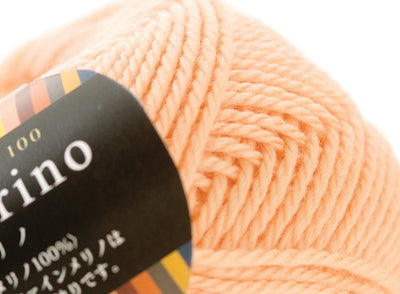 A 30g donut-style ball of Pierrot Fine Merino yarn. The image showcases the smooth, tightly spun plies of 100% Extra Fine Merino wool, reflecting the high-quality Japanese craftsmanship and the soft, matte finish characteristic of premium boutique yarns in apricot colour