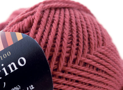 A 30g donut-style ball of Pierrot Fine Merino yarn. The image showcases the smooth, tightly spun plies of 100% Extra Fine Merino wool, reflecting the high-quality Japanese craftsmanship and the soft, matte finish characteristic of premium boutique yarns in antique rose