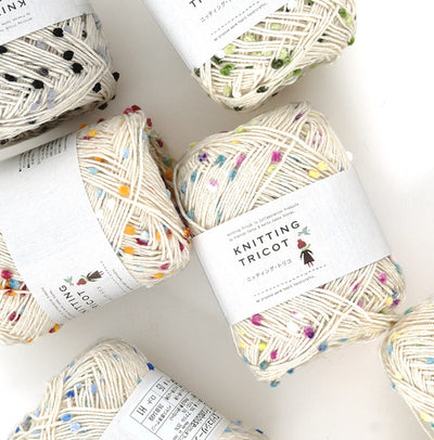 Several skeins of Pierrot Framboise yarn with multicolored speckles, arranged on a surface with labels indicating the brand and type.