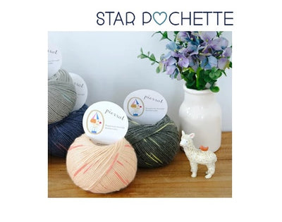 Pierrot Star Pochette yarn skeins in various colors displayed alongside a vase with flowers and a decorative sheep figure.
