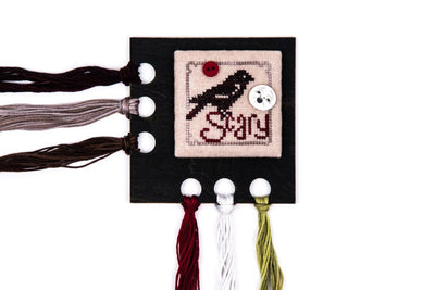 A professional-grade, square-shaped floss organizer titled 'Square-o-logy.' This high-definition tool is crafted from premium hardwood and measures 4 inches by 4 inches. It features 6 precision-drilled holes for thread organization. The central area is recessed or flat, designed specifically to hold a small, personal cross-stitch design for decoration