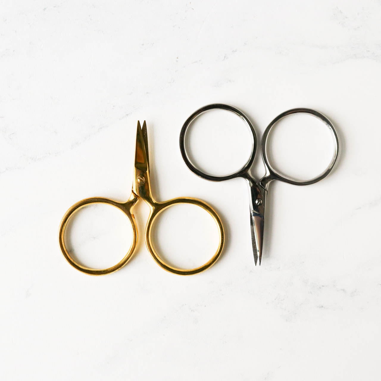 A pair of Putford Primitive miniature scissors featuring distinctively large circular finger holes and short, sharp blades. The scissors are shown in three vintage-inspired colors, highlighting their compact 2.5-inch size and handcrafted 'primitive' aesthetic, perfect for precise thread snipping