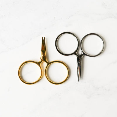 A pair of Putford Primitive miniature scissors featuring distinctively large circular finger holes and short, sharp blades. The scissors are shown in three vintage-inspired colors, highlighting their compact 2.5-inch size and handcrafted 'primitive' aesthetic, perfect for precise thread snipping