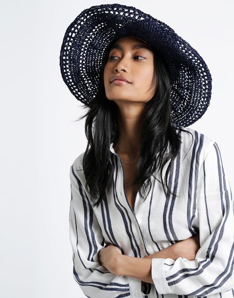 A person wearing a crocheted straw hat with a white shirt. The hat appears to be in Dark navy blue and has a wide brim.