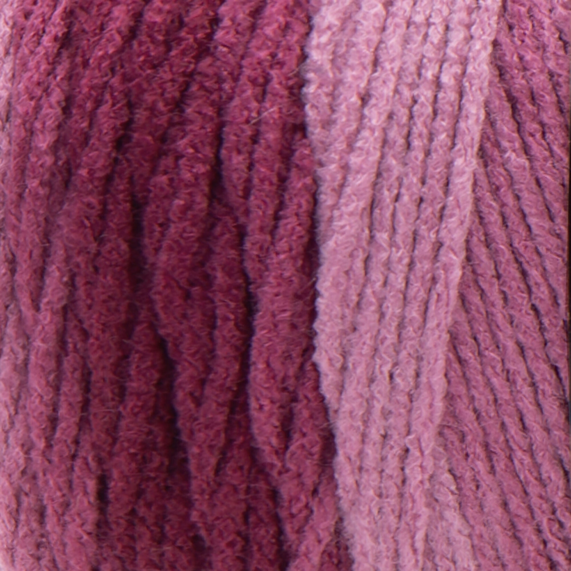 A large 283-gram skein of Red Heart Super Saver Ombre yarn, showing a beautiful gradient transition from a light tint to a deep, saturated shade of pink to red color. The yarn has a classic 4-ply twist and a soft matte finish, perfect for creating shawls, blankets, and garments with a natural ombré effect