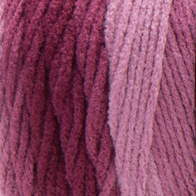 A large 283-gram skein of Red Heart Super Saver Ombre yarn, showing a beautiful gradient transition from a light tint to a deep, saturated shade of pink to red color. The yarn has a classic 4-ply twist and a soft matte finish, perfect for creating shawls, blankets, and garments with a natural ombré effect