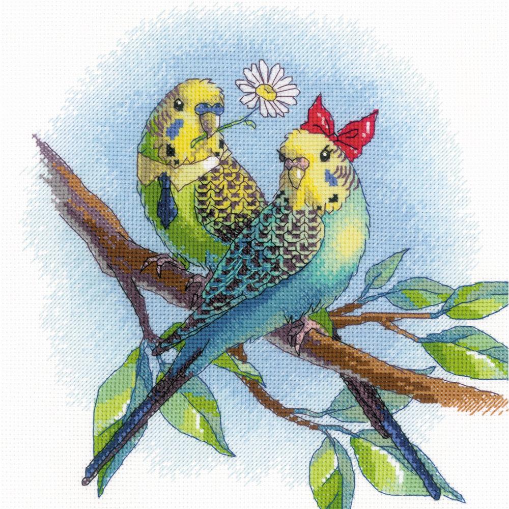 Cross stitch kit image depicting two colorful lovebirds on a tree branch with a daisy and a red bandana, surrounded by green leaves against a blue background.