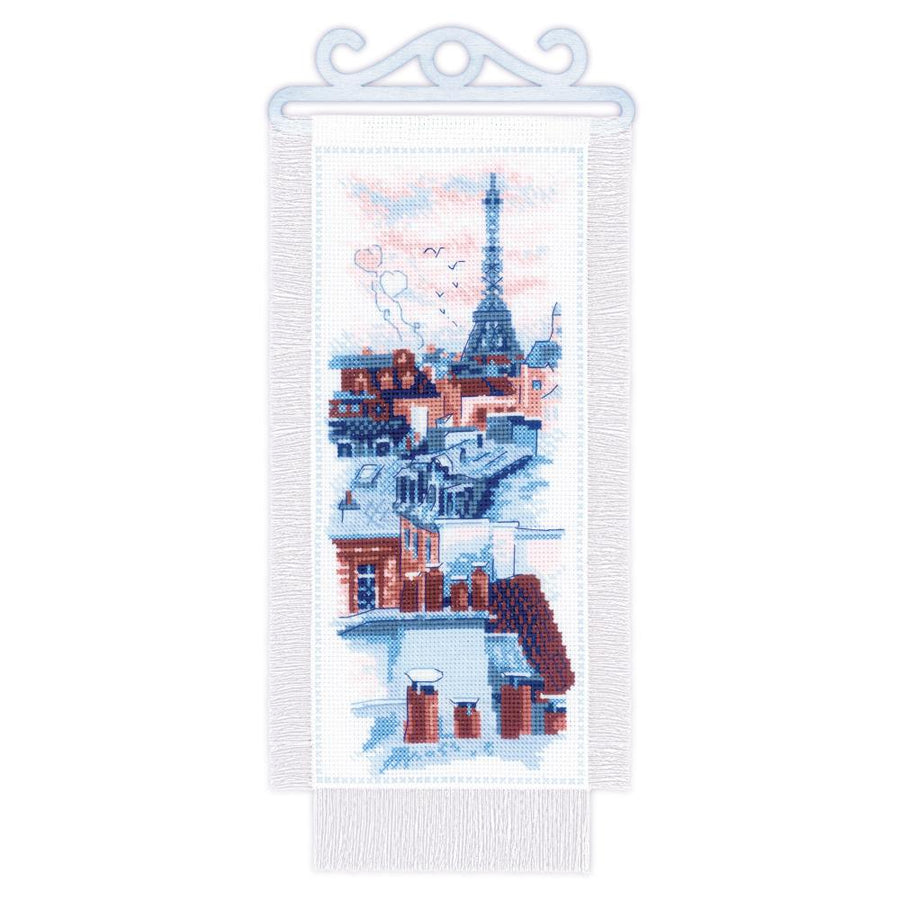 A scenic Riolis cross-stitch kit titled 'Paris Roofs,' featuring a panoramic vertical view of Parisian rooftops leading to the Eiffel Tower in the distance. The kit is worked on 14-count Aida fabric and includes a specialized wooden hanger to display the finished 15 x 31 cm piece in a rustic, artisanal style