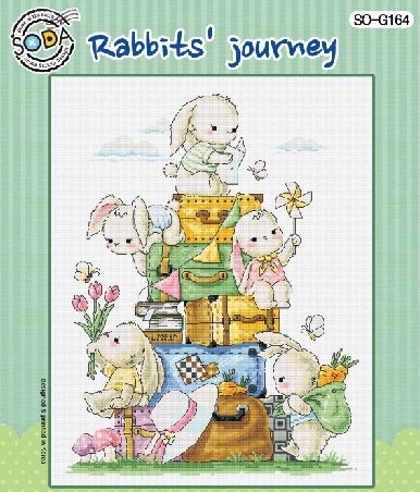 A vertical cross-stitch kit from SODA (Korea) titled 'Rabbit's Journey.' The design features a whimsical rabbit traveling through a charming landscape filled with tiny houses, trees, and creative vignettes. The kit includes 18-count white Aida cloth, full skeins of DMC embroidery threads, and a needle. The finished design measures 23 cm wide by 32 cm high