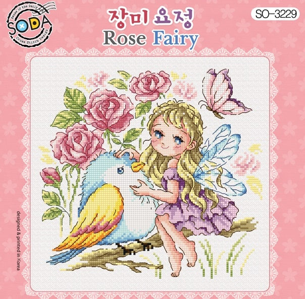 A slightly horizontal, rectangular cross-stitch kit from SODA (Korea) titled 'Rose Fairy.' The design features a whimsical illustration of a delicate fairy with translucent wings surrounded by large, blooming roses and greenery in a palette of romantic pinks, deep reds, and soft garden greens. The kit includes 14-count white Aida cloth, full skeins of DMC embroidery threads, and a needle. The finished design measures 20.5 cm by 19 cm