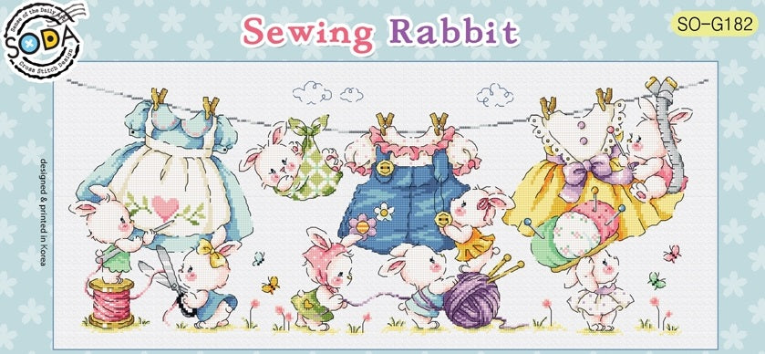 A large, panoramic cross-stitch kit by Korean designer SODA titled 'Sewing Rabbit.' The scene features several whimsical rabbits busy with sewing machines, yarn, and needlework tools. The kit includes 18-count white Aida cloth, full skeins of DMC embroidery threads, and a needle for a finished design measuring 286 by 115 stitches