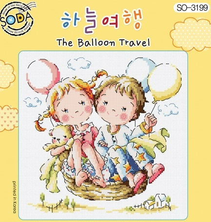A charming, square-format cross-stitch kit from SODA (Korea) titled 'The Balloon Travel.' The design features a colorful, whimsically decorated hot air balloon floating over a miniature village and rolling hills. The kit includes 14-count white Aida cloth, full skeins of DMC embroidery threads, and a needle. The finished design measures 19 cm wide by 18.5 cm high.