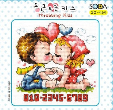 A cross stitch kit image depicting a cartoon-style man and woman kissing, with hearts and floral motifs around them. The kit is labeled with 'SODA' 