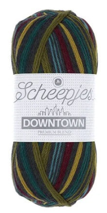 A skein of Scheepjes Downtown self-striping yarn in multicolor, predominantly in shades of dark mustard, dark blue, and olive green.