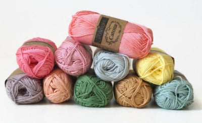 Scheepjes Catona 50g cotton balls; the ultimate yarn stash for colorful ripple blankets and mandalas. A collection of Scheepjes Catona yarn in various colors, displayed in a stacked arrangement with the brand label visible on top.