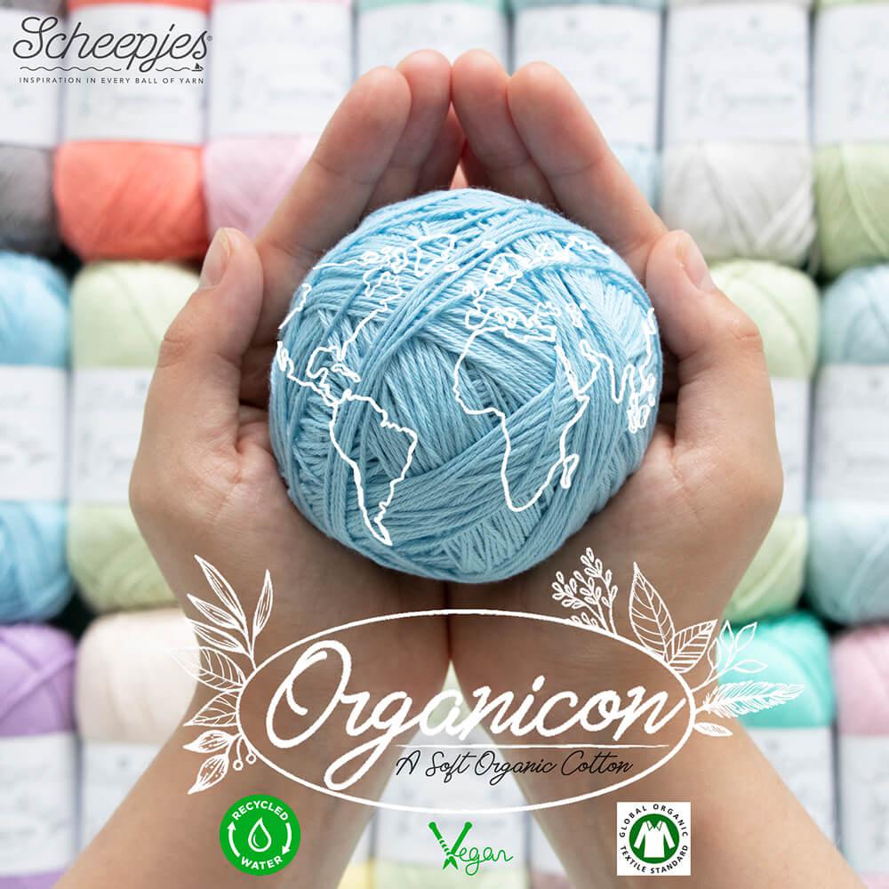 A person holding a ball of light blue yarn with 'Organicon' branding, with a background of various colored yarn.