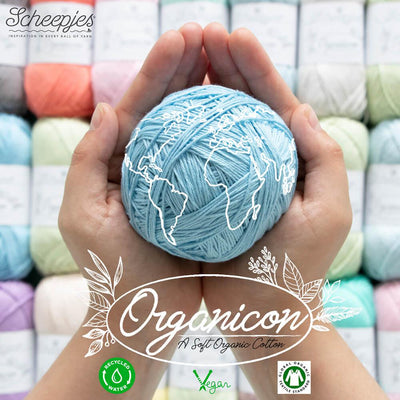 A person holding a ball of light blue yarn with 'Organicon' branding, with a background of various colored yarn.