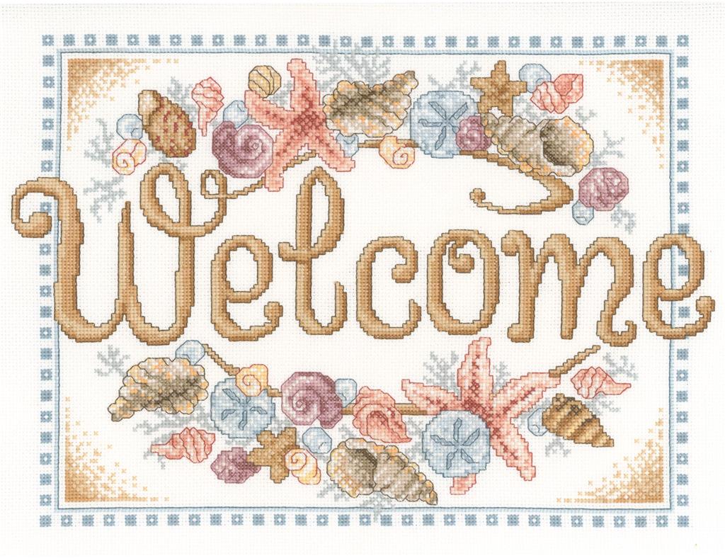 A bright and welcoming cross-stitch kit designed by Ursula Michael. The artwork features the word 'Welcome' surrounded by a variety of detailed seashells in coastal tones. The kit includes 14-count Aida fabric and full skeins of DMC embroidery threads to complete the nautical design