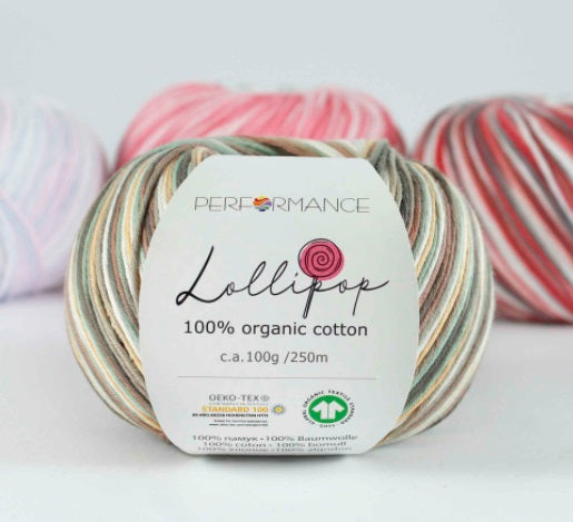 A skein of brown Lollipop brand organic cotton yarn with a label showing the brand name and yarn type, surrounded by other skeins of yarn in the background.