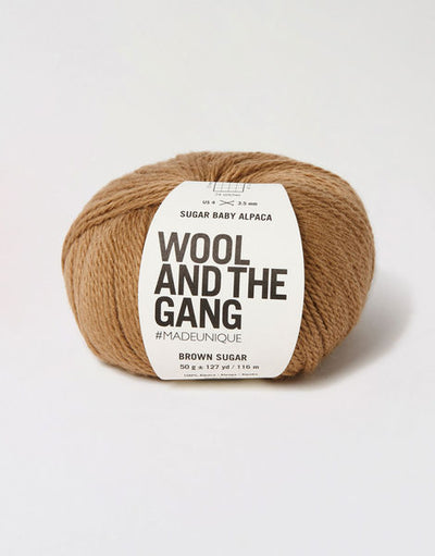 A blue skein of WOOL AND THE GANG Sugar Baby Alpaca yarn with a label in the center in brown sugar colour
