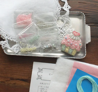 A flat-lay of the Beads Brooch Kit, highlighting the elegant designer packaging, organized bead packets, and the clear, step-by-step instructional guide