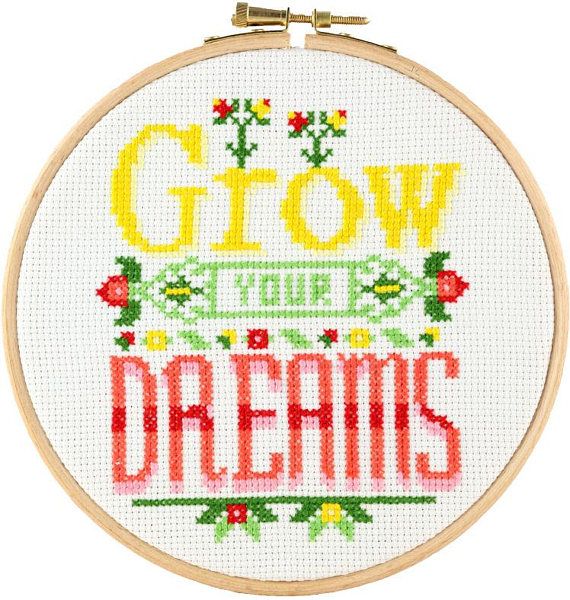 A complete beginner's cross-stitch kit from Stitchonomy titled 'Grow Your Dreams.' The design features a charming potted plant with vibrant green leaves and a motivational quote. Included in the package is a 6-inch embroidery hoop, 14-count white Aida fabric, earthy and bright embroidery floss, a needle, and clear instructions.