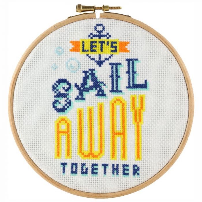 Cross stitch kit depicting a sailboat and the text 'Let's Sail Away Together' on a light background, framed in a light-colored border.