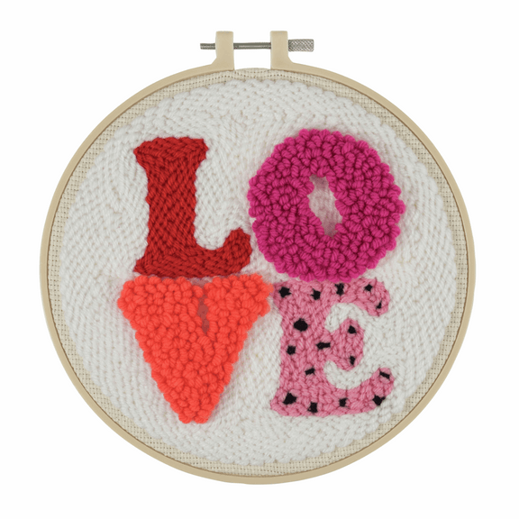 A complete 'Love' punch needle starter kit by Trimits. The kit features a 20.32cm (8-inch) non-slip plastic hoop, pre-printed 11-count punch needle fabric with a bold 'Love' motif, colorful yarns, a punch needle tool, and a needle threader. The finished artwork showcases a plush, looped texture in vibrant pink and red tones