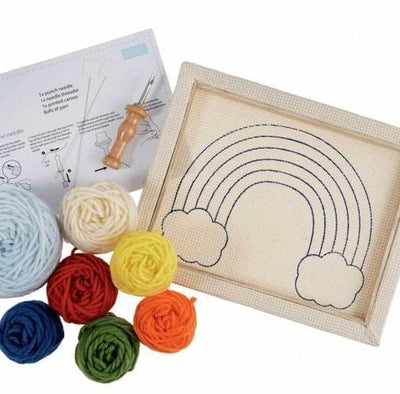 The kit includes an 8x10 inch fabric panel pre-stretched on a wooden frame with a printed rainbow outline. It comes with a multi-colored yarn palette, a specialized punch needle tool, a needle threader, and step-by-step instructions for creating a plush, looped texture