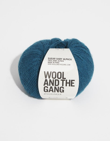 A blue skein of WOOL AND THE GANG Sugar Baby Alpaca yarn with a label in the center in blueish-green colour.