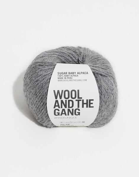 A blue skein of WOOL AND THE GANG Sugar Baby Alpaca yarn with a label in the center in tweed grey colour