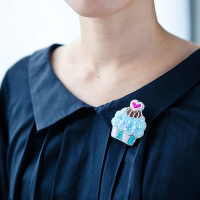 A person wearing a dark-colored shirt with a beaded brooch on the collar.