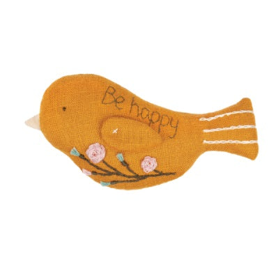 "A finished Aroma Bird tucked into a drawer of folded linens, highlighting its use as a stylish and fragrant sachet. On the bird it has "be happy" wordings and embroidered flowers design on it.