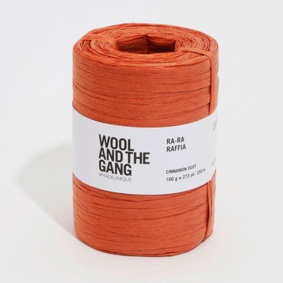 A roll of orange Wool And The Gang Ra-Ra Raffia yarn with a label in the center.